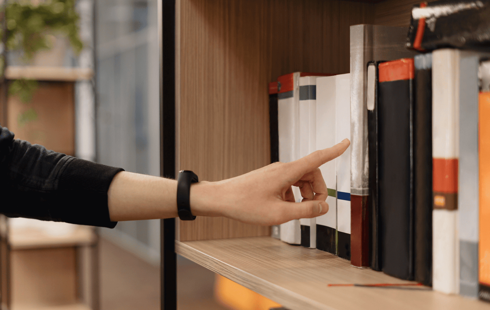 A person pointing at a book on a shelf, indicating interest or recommendation.